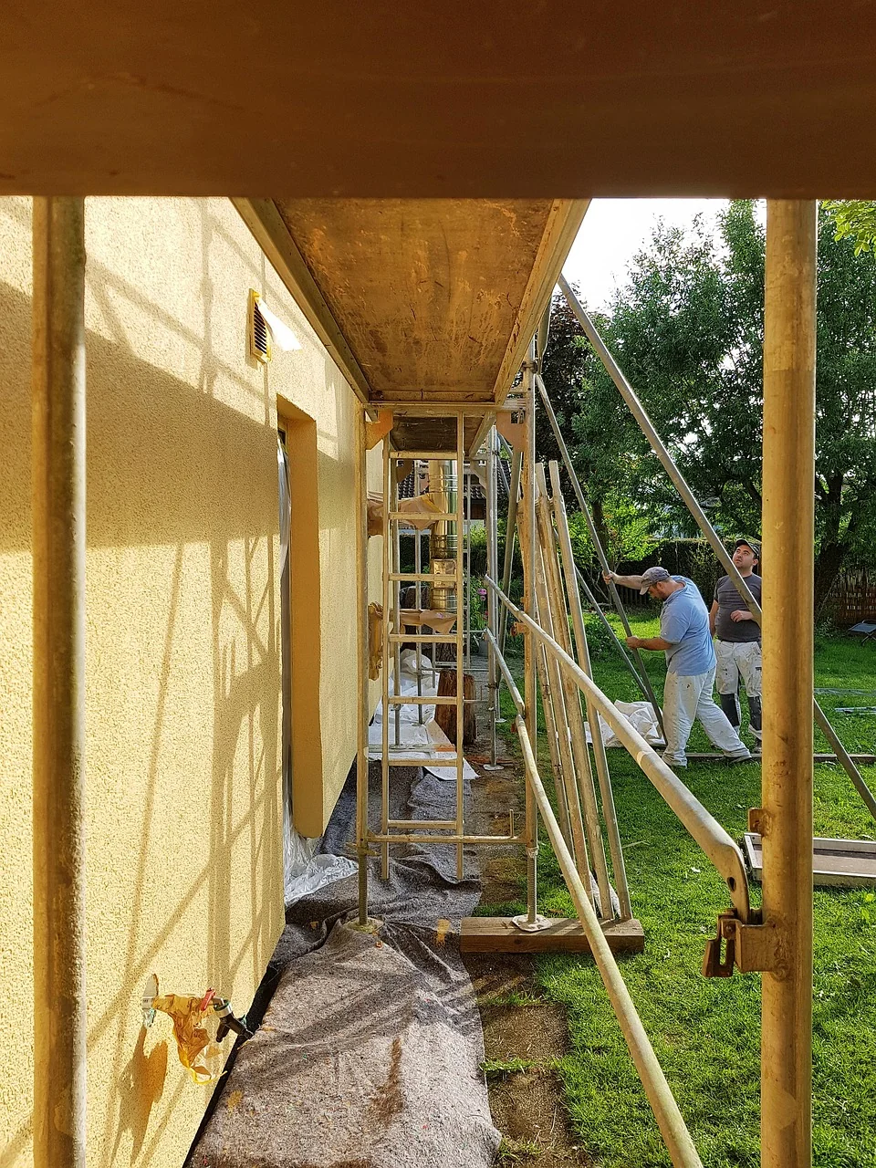 Plany architektoniczne i miarka na rusztowaniu przed remontowanym budynkiem, symbolizujące przygotowania do prac elewacyjnych.